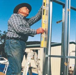 John on step ladder measuring a wall frame with spirit level